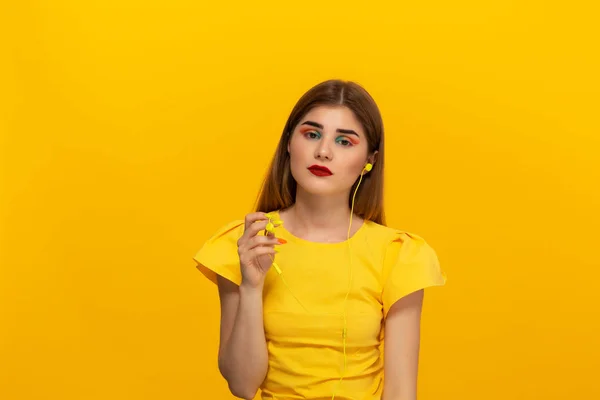 Jovem modelo feliz em um tee amarelo ouve música com fones de ouvido com fio em pé sobre fundo amarelo — Fotografia de Stock