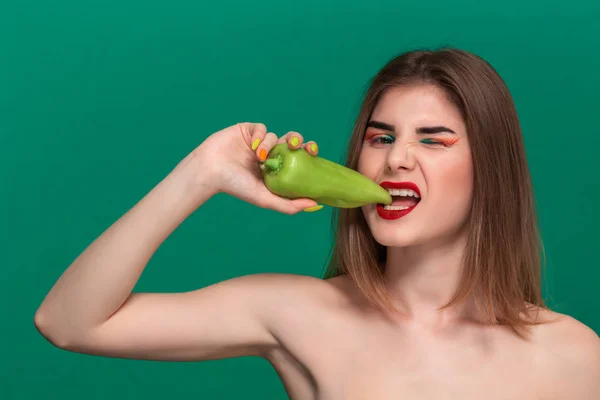 Retrato de close-up de bela jovem com maquiagem de cor brilhante segurando pimenta verde de pé isolado na frente de um fundo verde — Fotografia de Stock