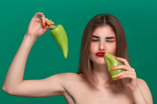 Крупный план портрет красивой молодой женщины с ярким цветом макияжа держа зеленый перец стоя изолированы перед зеленым фоном — стоковое фото