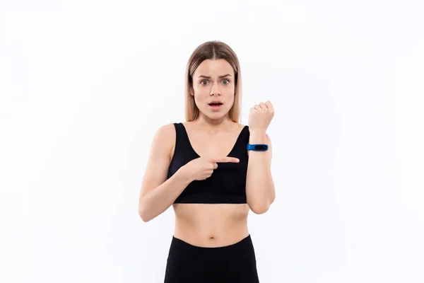 Ung sportig blond kvinna i en svart sportkläder förvånad kontroll puls med smarta klockor efter träningen stående över vit bakgrund — Stockfoto