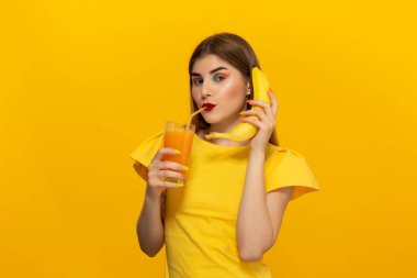 Sarı arka plan üzerinde izole yüz yakın ofange suyu ve muz cam tutan güzel bir genç kızın yakın çekim portre.