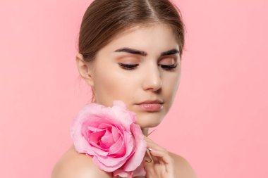 Pembe arka plan üzerinde izole pembe gül çiçeği ile güzel bir genç kızın yakın çekim portresi.