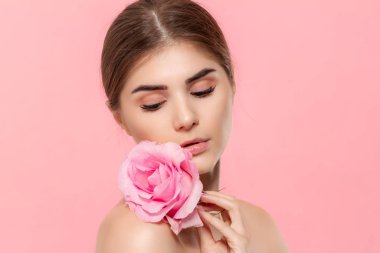Pembe arka plan üzerinde izole pembe gül çiçeği ile güzel bir genç kızın yakın çekim portresi.