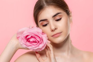 Pembe arka plan üzerinde izole pembe gül çiçeği ile güzel bir genç kızın yakın çekim portresi.