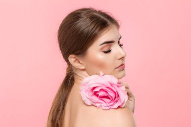 Pembe arka plan üzerinde izole pembe gül çiçeği ile güzel bir genç kızın yakın çekim portresi.