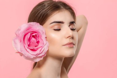 Pembe arka plan üzerinde izole pembe gül çiçeği ile güzel bir genç kızın yakın çekim portresi.