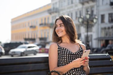 Siyah elbiseli güzel kız eski Avrupa kasabasında gezi turu sonra dinlenme akıllı telefon tutan bir bankta oturur.