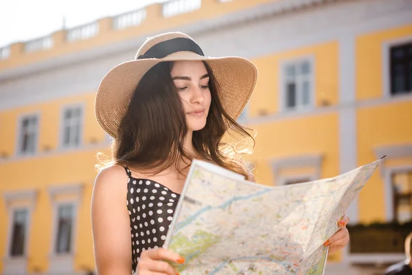 Pretty girl in a black dress and hat with wide flaps looks at the map finding route during sightseeing tour while traveling in the old European town. — Stock Photo, Image