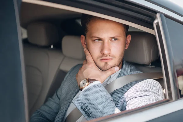 Retrato de un joven hombre de negocios en un traje en el asiento trasero . — Foto de Stock