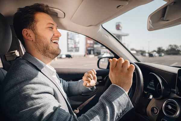 Ευτυχισμένος οδηγός σε ένα κουστούμι που χορεύει στο δικό του αμάξι ακούγοντας μουσική και. — Φωτογραφία Αρχείου