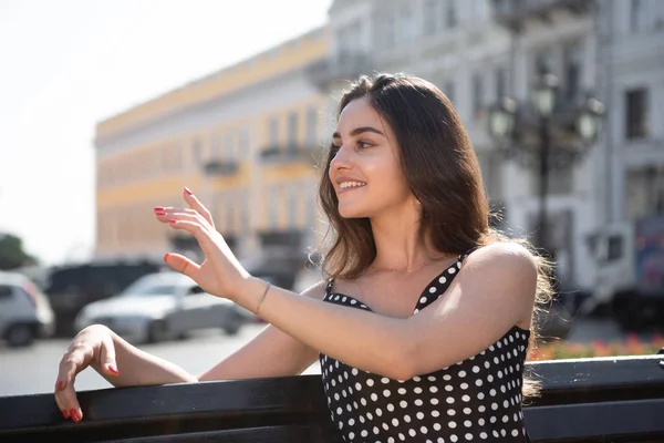 Hermosa joven con un vestido negro se sienta en un banco descansando después de un recorrido por la ciudad vieja europea . — Foto de Stock