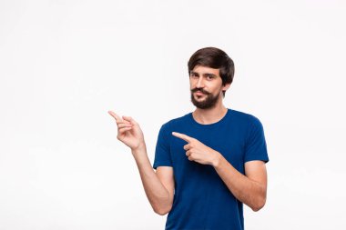 Sakallı mavi gömlekli yakışıklı brunet adam ve bıyıkları parmaklarıyla sol köşeye beyaz arka plan üzerinde izole ayakta işaret. Ürün ve reklam yeri.