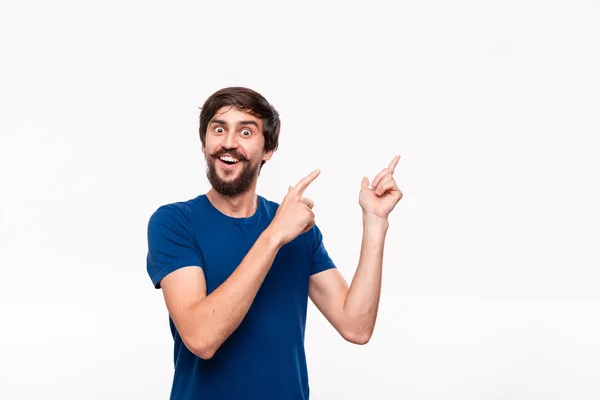 青いシャツにあごひげと口ひげを持つハンサムなブルネットの男は、白い背景の上に孤立して立って左隅に指で指を指しています。製品と広告の場所. — ストック写真