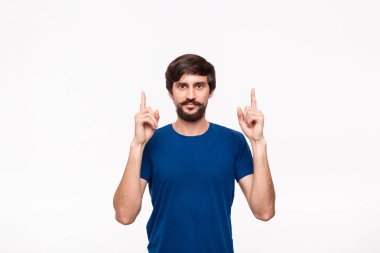 Sakallı mavi gömlekli yakışıklı brunet adam ve bıyıkları parmaklarıyla beyaz arka plan üzerinde izole ayakta işaret. Ürün ve reklam yeri.