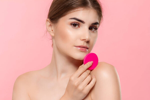 Красивая модель яблоки косметический продукт к коже с розовой губки хлопка изолированы на розовом фоне. Модель смотрит в камеру
.