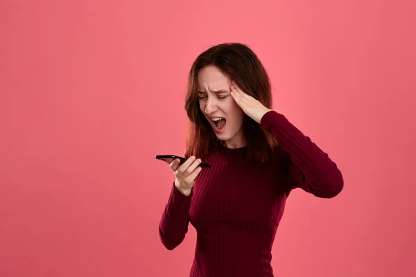 Porträt eines schönen brünetten Mädchens, das auf dunkelrosa Hintergrund steht und besorgt schaut, während es am Telefon spricht. — Stockfoto