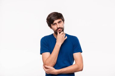 Mavi gömlekli düşünceli yakışıklı brunet adam kollarını göğsüne katlanmış tutan ve beyaz arka plan üzerinde izole ayakta yüz bir el yakın tutmak.