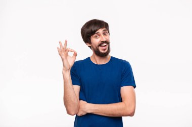 Yakışıklı brunet sakallı adam mavi gömlek bıyıklı ok işareti gösteren beyaz arka plan üzerinde izole ayakta. Tamam hareketi.