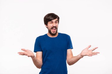 Sakallı mavi gömlekli ve çoğu ağrılı, beyaz arka plan üzerinde izole ayakta duran şaşıran omuzlarını silkme iyi görünümlü brunet adam. Duygu ve şok jest.