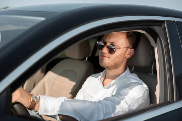 Ο ευτυχισμένος οδηγός με άσπρο πουκάμισο και γυαλιά ηλίου οδηγεί το αμάξι του. Έννοια της επιτυχίας. — Φωτογραφία Αρχείου
