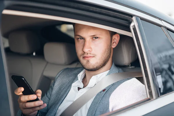 Retrato de un joven hombre de negocios en un traje en un asiento trasero comprobando las noticias con el teléfono inteligente — Foto de Stock