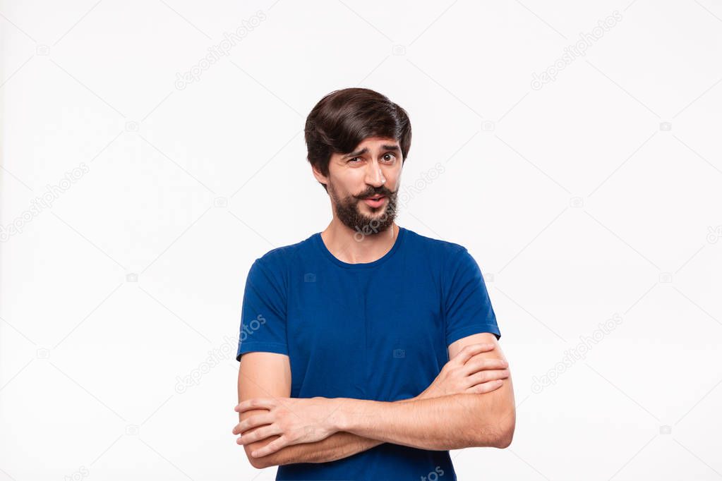 Handsome brunet man in a blue shirt holding arms folded over his chest with sceptical emotion standing isolated over white background.