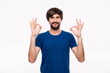 Beyaz arka plan üzerinde izole duran iki eliyle Ok işareti jest gösteren mavi gömlek bıyıklı yakışıklı brunet sakallı adam.