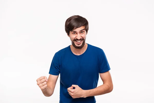 Giovane uomo barbuto bruno con i baffi in una camicia blu posa esprimendo gesto di vittoria con le braccia in piedi isolato su sfondo bianco . — Foto Stock