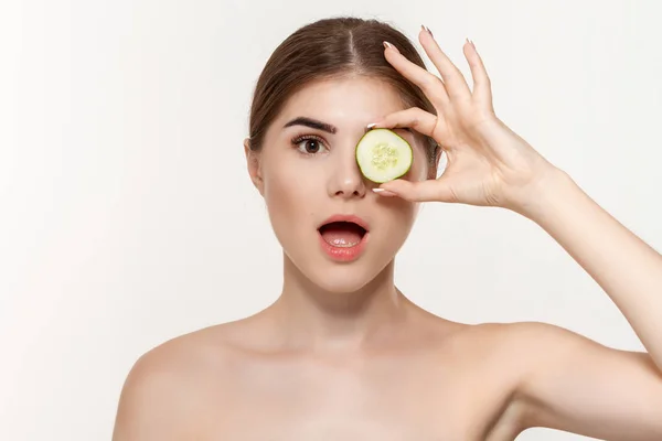 Close-up retrato de uma bela jovem segurando fatias de pepino verde perto de olhos isolados sobre fundo branco . — Fotografia de Stock