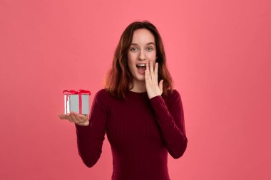 Heyecanlı güzel esmer kız koyu pembe arka plan üzerinde izole ayakta ve kameraya gülümseyen bir kurdele ile mevcut kutu tutan. Özel etkinliği kutluyoruz.