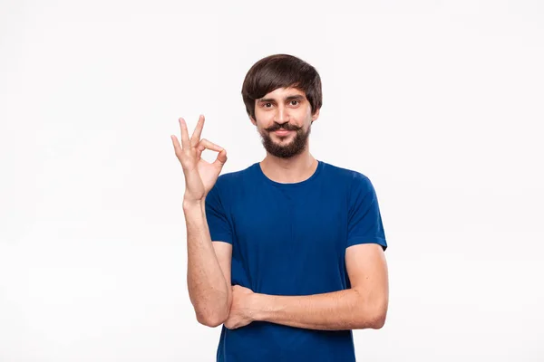 Przystojny Brunet Brodaty człowiek z wąsami w niebieskiej koszulce pokazując gest OK znak stojący izolowane na białym tle. — Zdjęcie stockowe