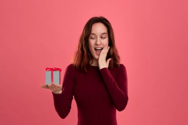 Heyecanlı güzel esmer kız koyu pembe arka plan üzerinde izole duran bir kurdele ile mevcut kutu tutan ve kameraya gülümseyerek.