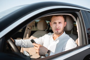 Araba sürerken cep telefonuna bakan gülümseyen genç işadamı.