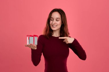 Mutlu güzel esmer kız koyu pembe bir arka plan üzerinde izole duran bir kurdele ile mevcut kutuyu işaret.