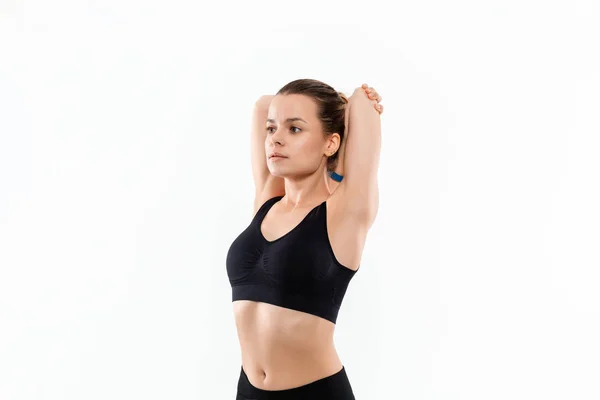 Joven mujer rubia deportiva en una ropa deportiva negro estiramiento antes de hacer ejercicio aislado sobre fondo blanco . — Foto de Stock