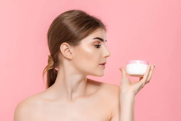 Güzel kız cildi nemlendirmek için krem tüp tutan. Model pembe arka plan üzerinde izole kamera bakar. Güzellik ve sağlık tedavisi kavramı.