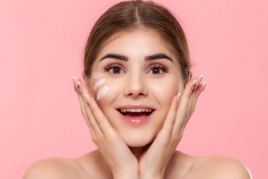 Mutlu güzel model pembe arka plan üzerinde izole kamera bakar. Cilde uygulanan nemlendirici hyaluronik krem.