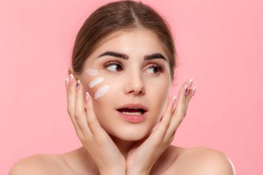 Mutlu güzel model pembe arka plan üzerinde izole. Cilde nemlendirici hyaluronik krem uygulanır. Güzellik ve sağlık tedavisi kavramı.