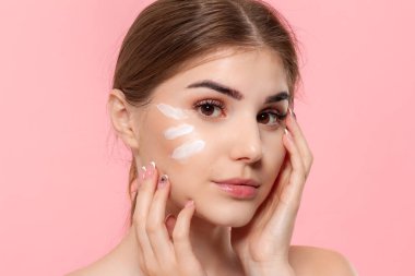 Güzel model pembe arka plan üzerinde izole bir hyaluronik krem beyaz tüp tutan cilde nemlendirici kozmetik ürün uygular. Güzellik ve sağlık tedavisi kavramı.