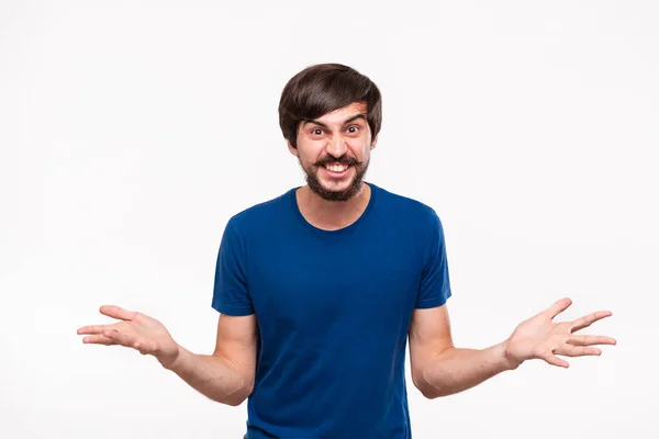 Bello sguardo brunet uomo in una camicia blu con barba e baffi urlando scuotendo le spalle essere sorpreso in piedi isolato su sfondo bianco . — Foto Stock