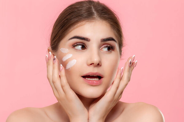 Happy beautiful model isolated over pink background. Moisturizing hyaluronic cream applied to skin. Concept of beauty and health treatment.