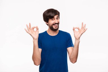 Beyaz arka plan üzerinde izole duran iki eliyle Ok işareti jest gösteren mavi gömlek bıyıklı yakışıklı brunet sakallı adam.