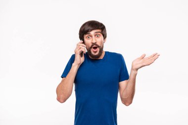 Sakallı mavi gömlekli pretty brunet adam ve çoğu ağrıları beyaz arka plan üzerinde izole duran kamera bakarak akıllı telefon tutarak şok. Sürpriz duygusu. Telefondan beklenmeyen haberler.