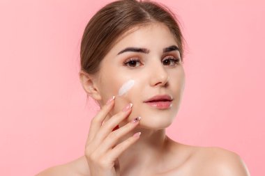 Güzel model pembe arka plan üzerinde izole bir hyaluronik krem beyaz tüp tutan cilde nemlendirici kozmetik ürün uygular. Güzellik ve sağlık tedavisi kavramı.