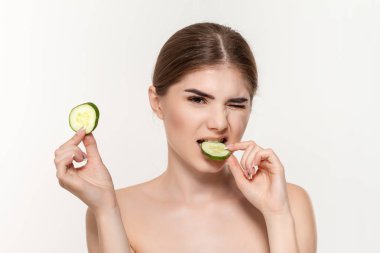 Beyaz arka plan üzerinde izole yeşil salatalık dilim ısırma güzel bir genç kız yakın çekim portre. Güzellik ve sağlık kavramı.