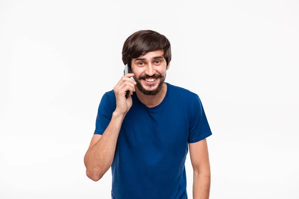 Bello uomo brunetta in camicia blu con barba e baffi sorridente parlando sullo smartphone in piedi isolato su sfondo bianco. Concetto di comunicazione — Foto Stock