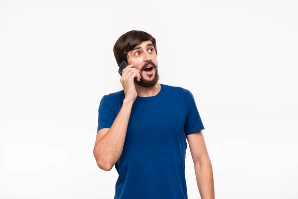 青いシャツにあごひげを生やしたハンサムなブルネットの男は、白い背景の上に孤立したスマートフォンで話す笑顔を見せた。コミュニケーションの概念 — ストック写真
