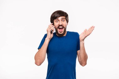 Sakallı mavi gömlekli pretty brunet adam ve çoğu ağrıları beyaz arka plan üzerinde izole duran kamera bakarak akıllı telefon tutarak şok. Sürpriz duygusu. Telefondan beklenmeyen haberler.