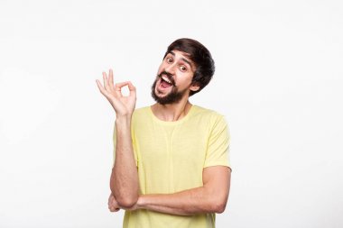 Yakışıklı brunet sakallı adam sarı gömlek bıyıklı ok işareti gösteren beyaz arka plan üzerinde izole ayakta. Tamam hareketi.