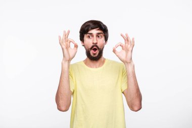 Yakışıklı brunet sakallı adam sarı gömlek bıyıklı ok işareti gösteren iki eli beyaz arka plan üzerinde izole ayakta. Tamam hareketi.